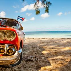 Voiture américaine ancienne rouge garée sur une plage de sable blanc bordée par la mer des Caraïbes à Cuba.