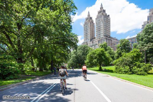 Balade new-yorkaise en petit groupe : promenade guidée à vélo dans les allées de Central Park Cyclistes effectuant une balade à vélo le long des allées verdoyantes de Central Park avec les immeubles de Manhattan en arrière-plan lors d'un séjour à New York.
