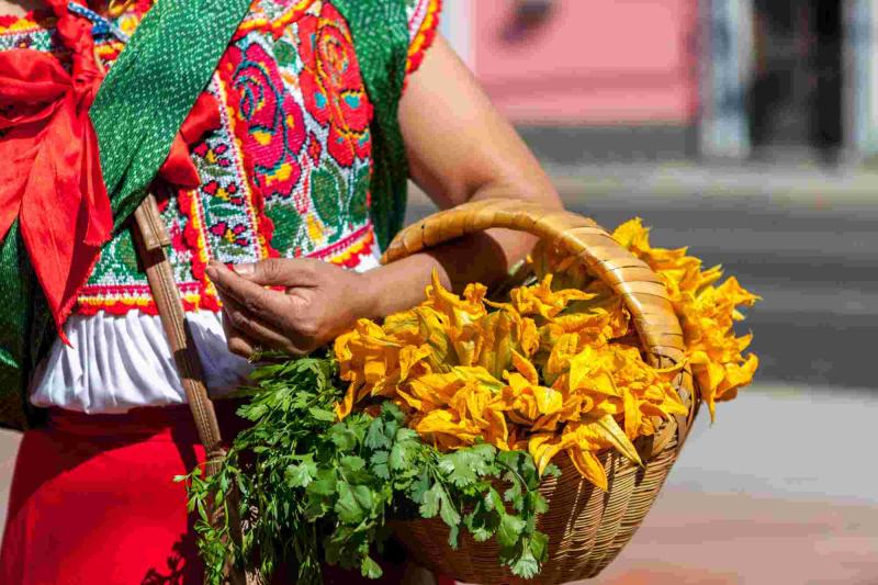 Femme mexicaine en tenue traditionnelle brodee portant un panier tressant garni de fleurs