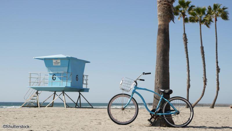 Circuit Ouest Américain en famille : promenade à vélo le long des plages de Los Angeles Un vélo bleu posé près d'un palmier et d'une cabane de sauvetage en bois bleu sur la plage de Santa Monica ou Venice Beach à Los Angeles.